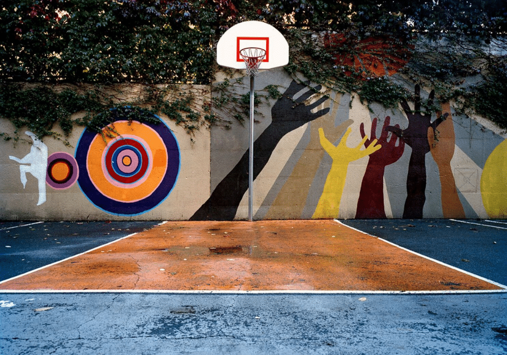 An outdoor basketball hoop set against a wall of colorful murals.